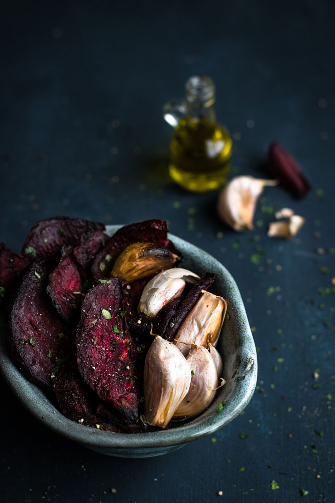 tigela com beterrabas e dentes de alho assados em primeiro plano, com ingredientes ao fundo 